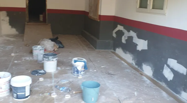 Local diafano con zócalo gris a medio pintar y botes de pintura en el suelo