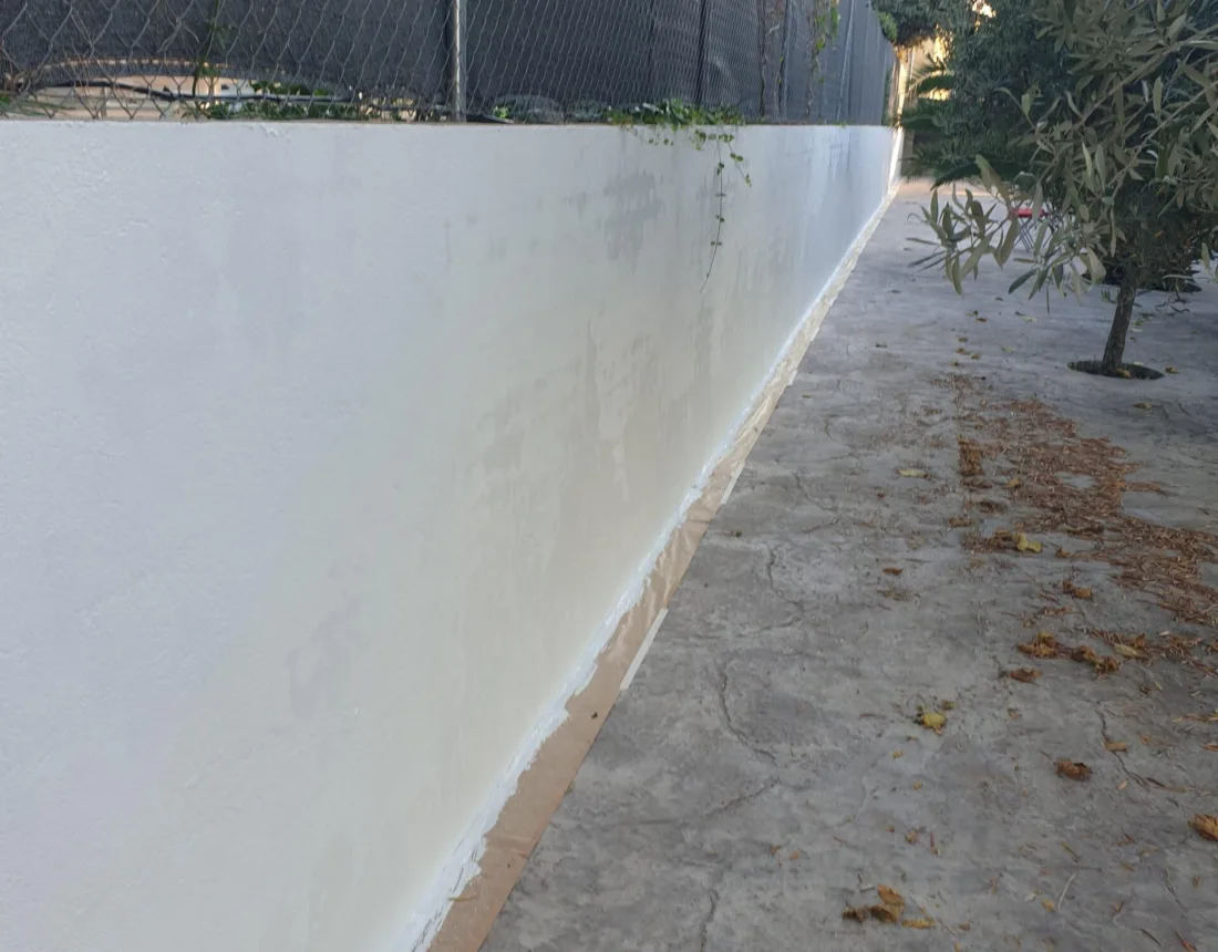 Muro largo de cerramiento recién pintado en blanco junto a la valla de la parcela