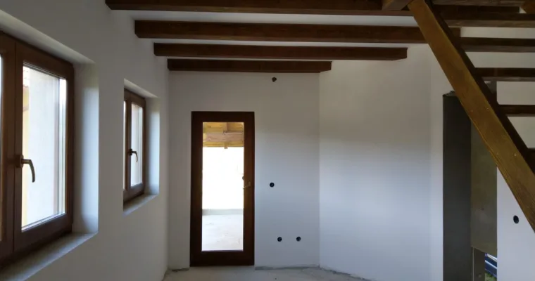 Estancia de obra nueva con vigas de madera vistas, ventanas de madera y escalera, recién pintada en blanco