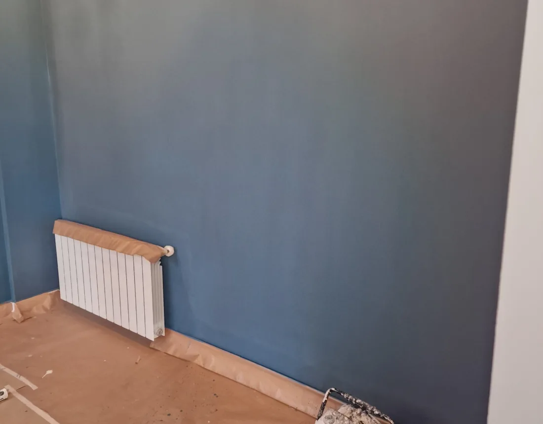 Pared pintada en azul con el radiador y el suelo protegidos
