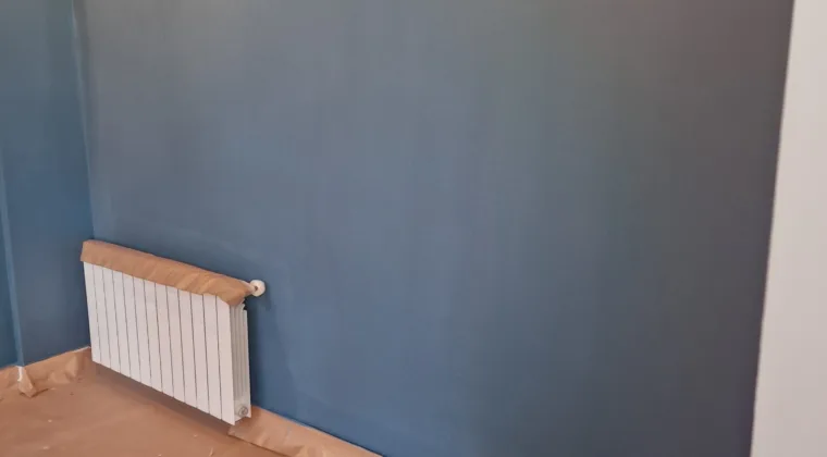 Pared pintada en azul con el radiador y el suelo protegidos