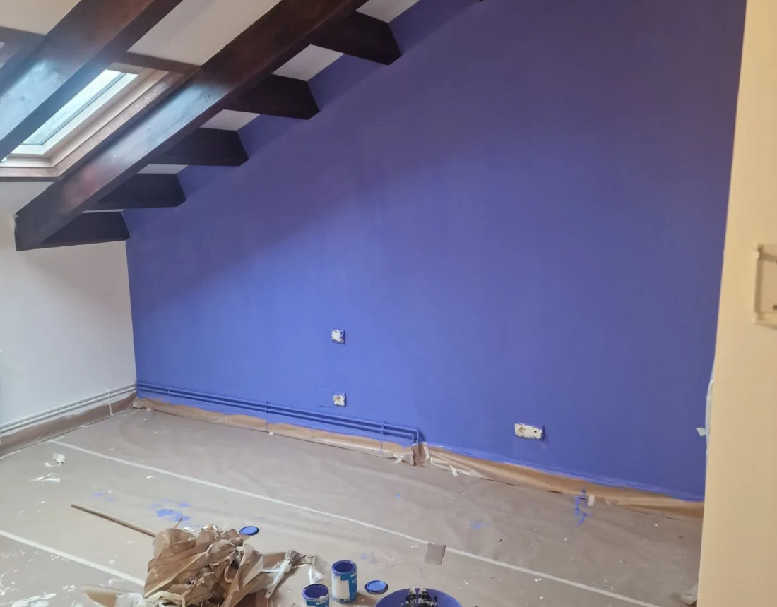 Pared pintada en morado bajo techo de vigas de madera en una buhardilla
