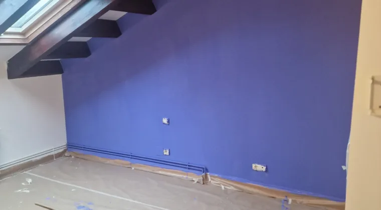 Pared pintada en morado bajo techo de vigas de madera en una buhardilla