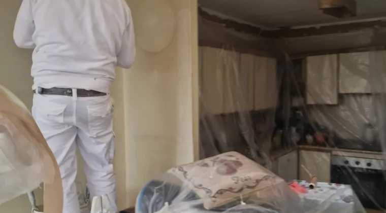 Pintor de espaldas pintando el techo de una cocina con los muebles cubiertos
