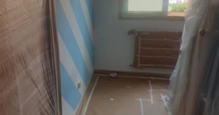 Habitación con papel pintado de rayas azules a medio retirar, en un piso de Collado Villalba