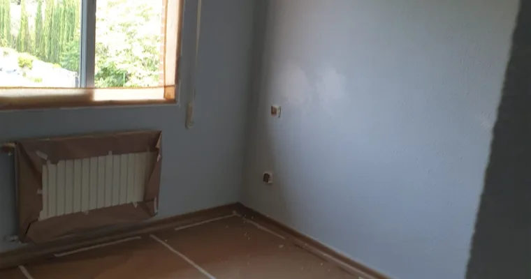 Dormitorio pintado en gris azulado con el radiador y el suelo aún protegidos, en Los Arroyos